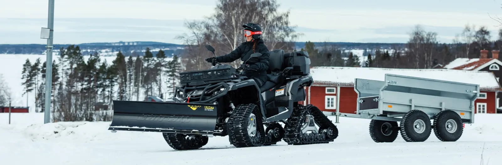 Fyrhjuling med plog och band drar en släpvagn i snön