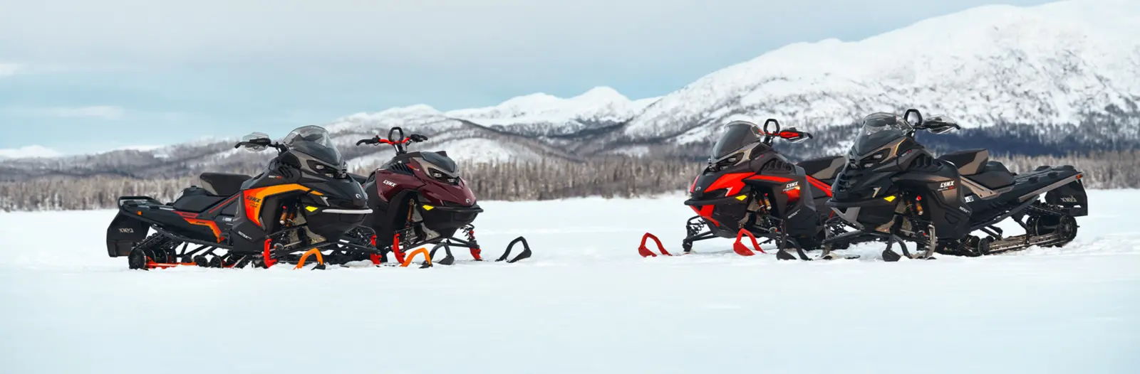 Fyra Lynx-snöskotrar på ett snöfält framför fjäll